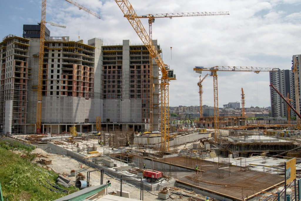 Eine große Baustelle mit mehreren Baukränen und im Bau befindlichen Hochhäusern. Die Baustelle ist weit fortgeschritten, und es sind viele Bauarbeiten im Gange.